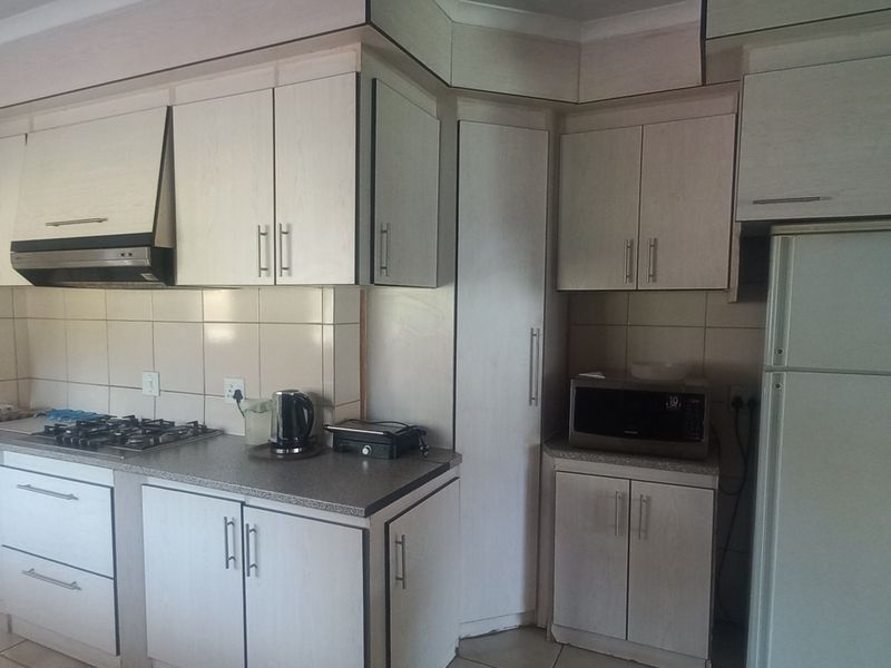 A functional kitchen featuring light-toned built-in cabinetry, a gas hob with extractor fan, tiled splashbacks, and an arched entryway leading to an adjacent space.