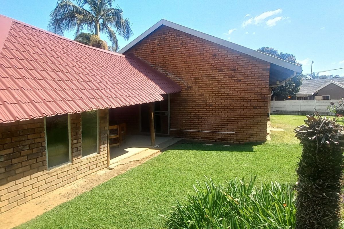 Rear view of a face brick house featuring a red metal roof, a covered patio area, and a well-maintained garden lawn.