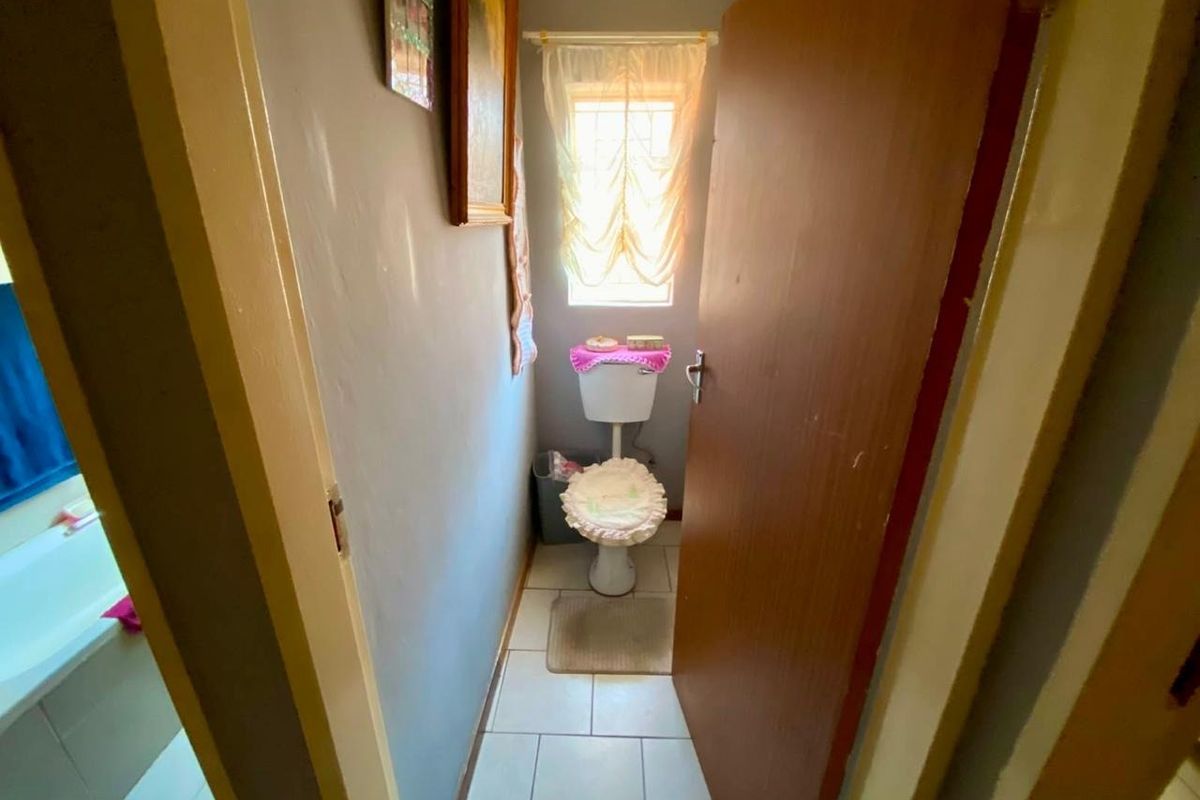 A compact bathroom featuring a standard toilet, tiled flooring, and a window providing natural light.