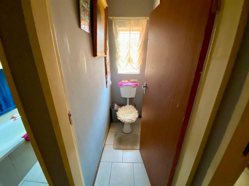 A compact bathroom featuring a standard toilet, tiled flooring, and a window providing natural light.