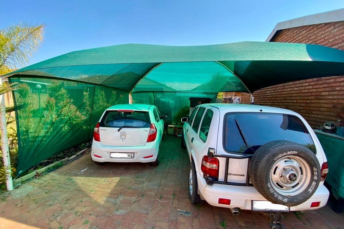 Outdoor carport area featuring a green shade cloth structure over a brick paved driveway, providing covered parking space.