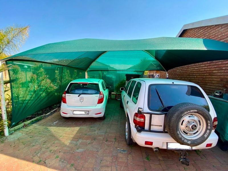 Outdoor carport area featuring a green shade cloth structure over a brick paved driveway, providing covered parking space.