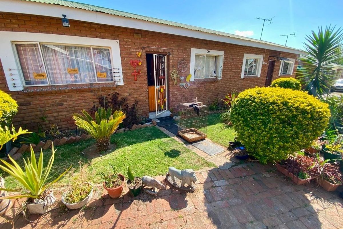 Front view of a single-story townhouse featuring a classic brick facade, corrugated metal roof, and a small front garden with a paved walkway.