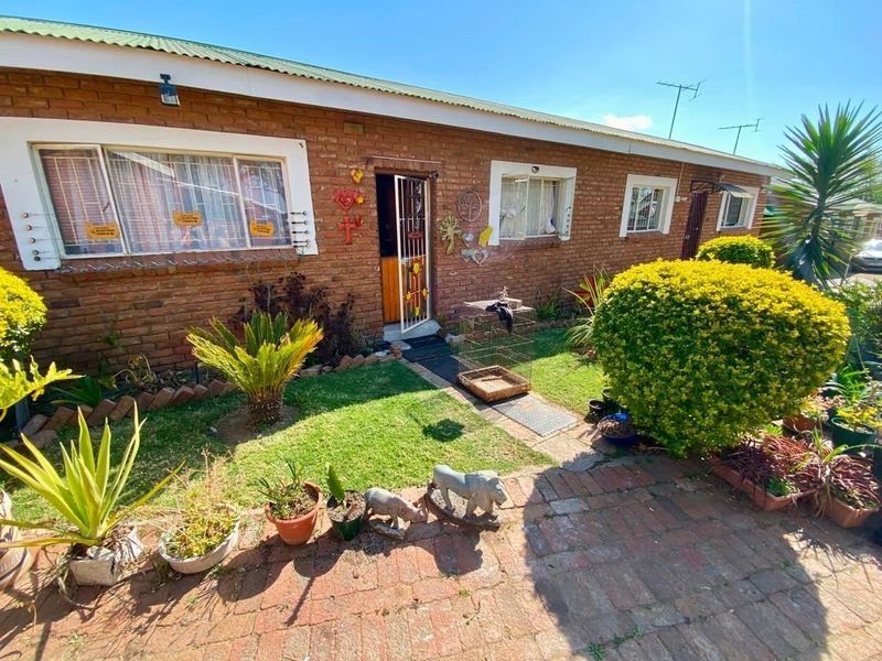 Front view of a single-story townhouse featuring a classic brick facade, corrugated metal roof, and a small front garden with a paved walkway.