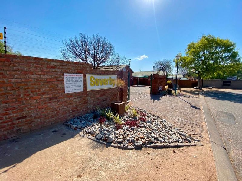 Entrance view of the Soverby townhouse complex featuring a brick boundary wall, electric fencing, and a paved driveway with landscaped rock garden.