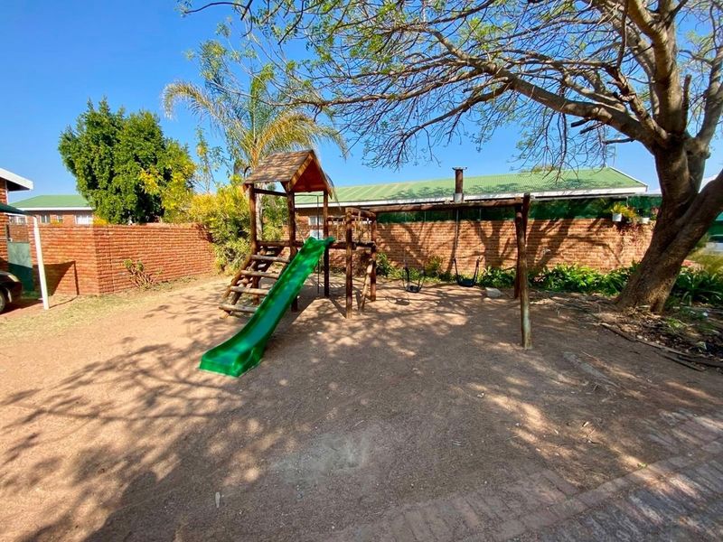A private backyard garden area featuring a brick boundary wall, mature tree, and a dedicated play area with a slide and swings.