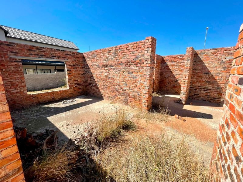 An unfinished residential structure featuring exposed brick walls and a concrete slab foundation, currently in a shell state awaiting completion.