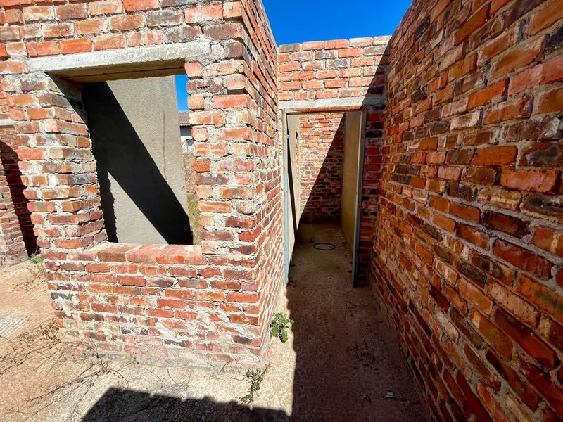 An unfinished residential structure featuring exposed brick walls and concrete lintels, currently in the early stages of construction.