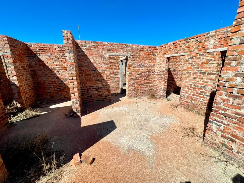 An unfinished residential structure featuring exposed brick walls and concrete lintels, currently in a shell state awaiting completion.