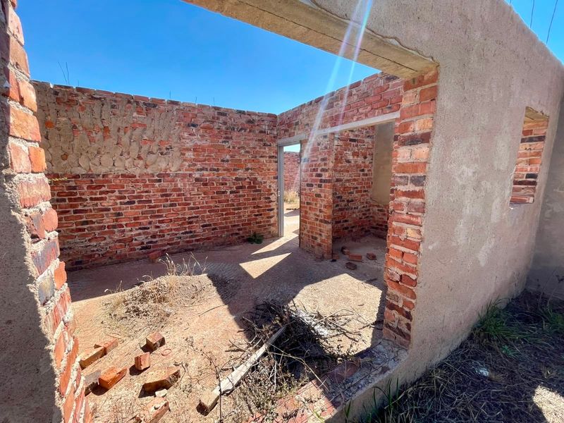 An unfinished residential structure featuring exposed brick walls and concrete lintels, currently in a shell state requiring significant completion work.