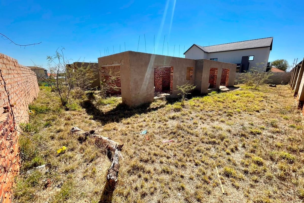 A view of a vacant residential plot featuring an unfinished masonry structure and brick boundary walls, requiring significant completion and landscaping.