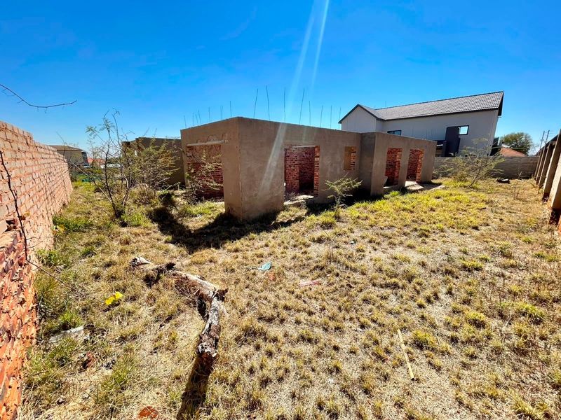 A view of a vacant residential plot featuring an unfinished masonry structure and brick boundary walls, requiring significant completion and landscaping.