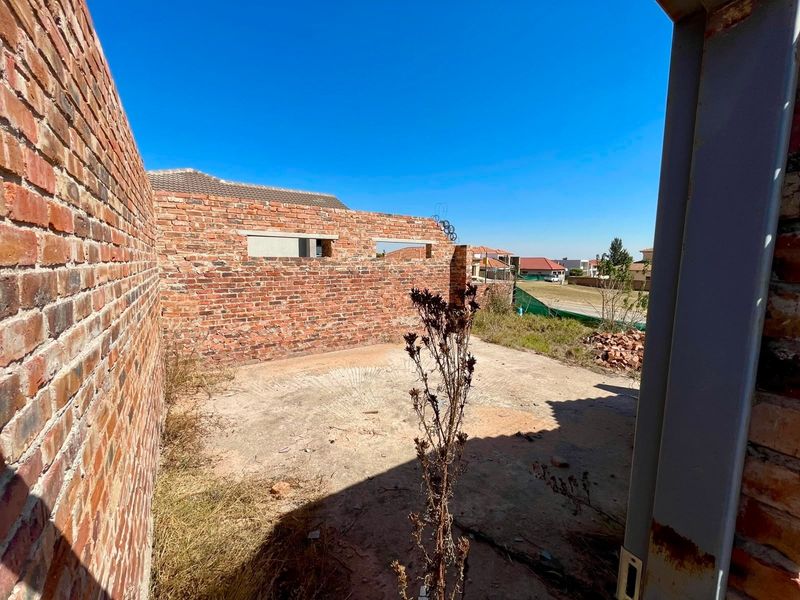 An unfinished residential construction site featuring exposed brick walls and a concrete slab foundation, set within a developing neighborhood.
