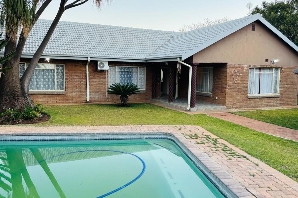 Rear view of a brick house featuring a swimming pool, paved walkway, and a covered porch area with established garden surroundings.