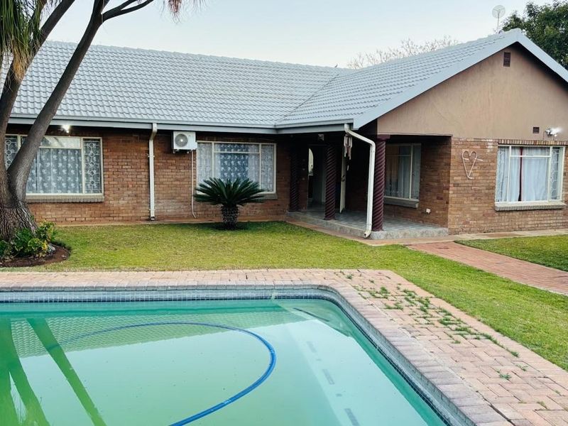 Rear view of a brick house featuring a swimming pool, paved walkway, and a covered porch area with established garden surroundings.