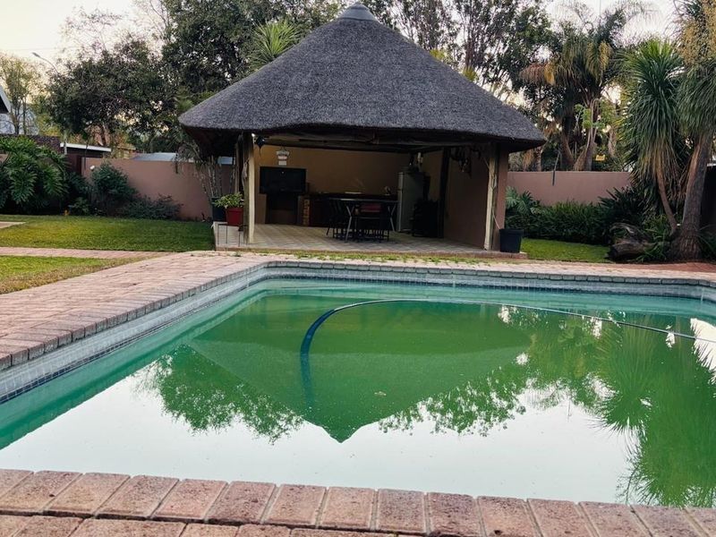 Outdoor pool area featuring a swimming pool with brick coping and a thatched lapa entertainment structure in the rear garden.