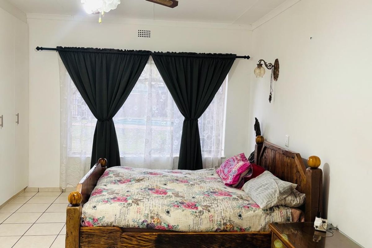 A bedroom featuring tiled flooring, built-in cupboards, and a ceiling fan, offering a functional space with neutral finishes.