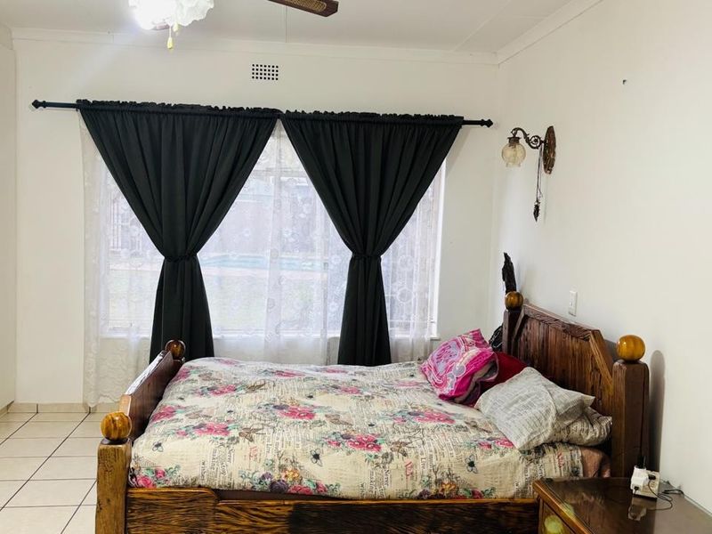 A bedroom featuring tiled flooring, built-in cupboards, and a ceiling fan, offering a functional space with neutral finishes.