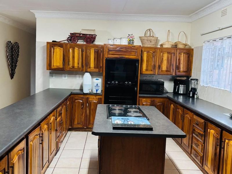 A functional kitchen featuring extensive wooden cabinetry, dark laminate countertops, a central island with an electric hob, and tiled flooring.