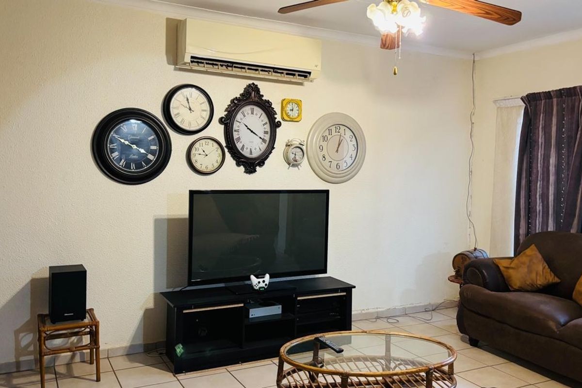 A living room featuring tiled flooring, a ceiling fan, and a wall-mounted split-system air conditioner.