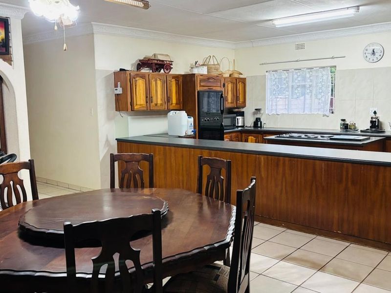 Open-plan kitchen and dining area featuring wooden cabinetry, built-in oven, hob, and tiled flooring, offering a functional layout for family living.