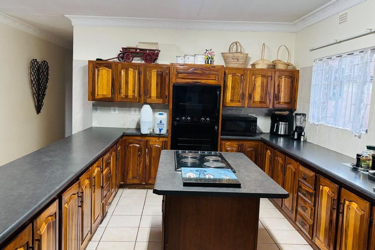 A functional kitchen featuring extensive wooden cabinetry, dark laminate countertops, a central island with an electric hob, and tiled flooring.