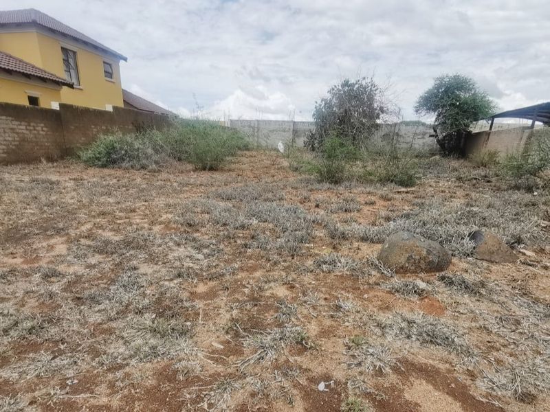 A vacant residential plot featuring natural ground cover and perimeter boundary walls, offering a blank canvas for future development.