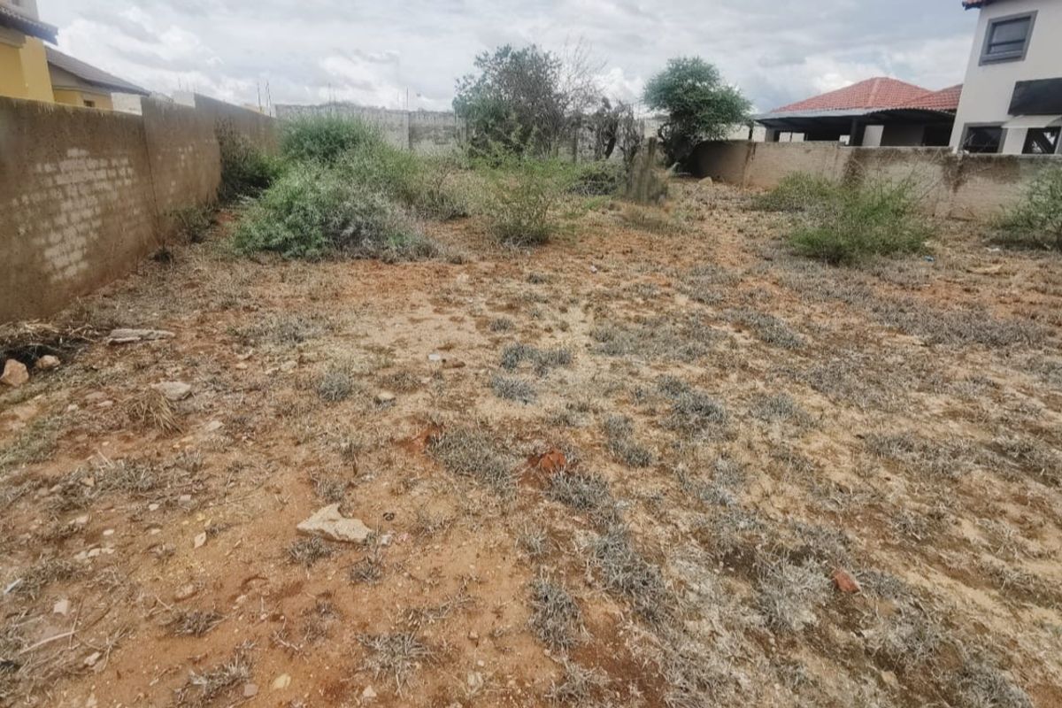 A vacant residential plot featuring a perimeter boundary wall and natural ground cover, suitable for future development.