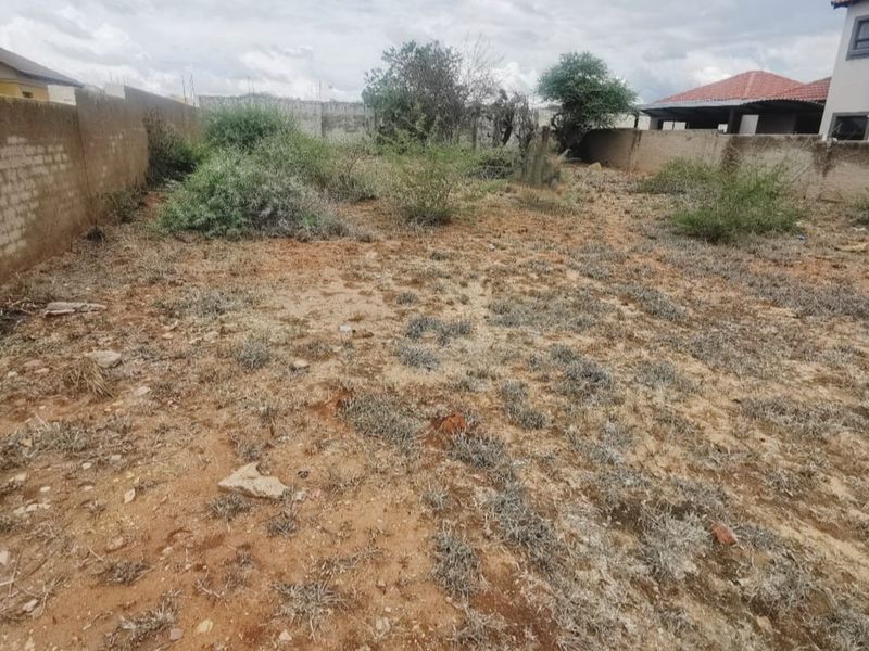 A vacant residential plot featuring a perimeter boundary wall and natural ground cover, suitable for future development.