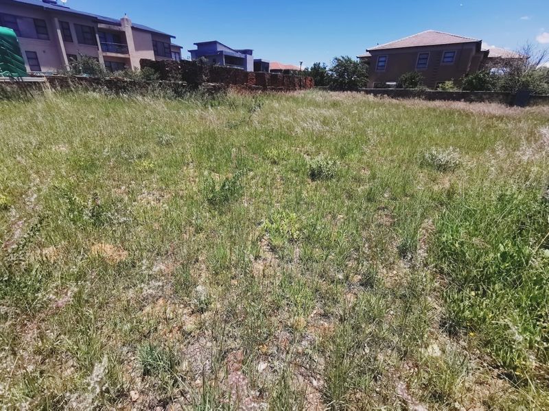 A vacant residential plot featuring overgrown grass and established boundary walls, situated within a developed neighborhood.