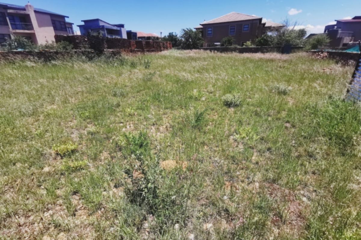 A vacant residential plot featuring overgrown grass and established boundary walls, situated within a developed neighborhood setting.