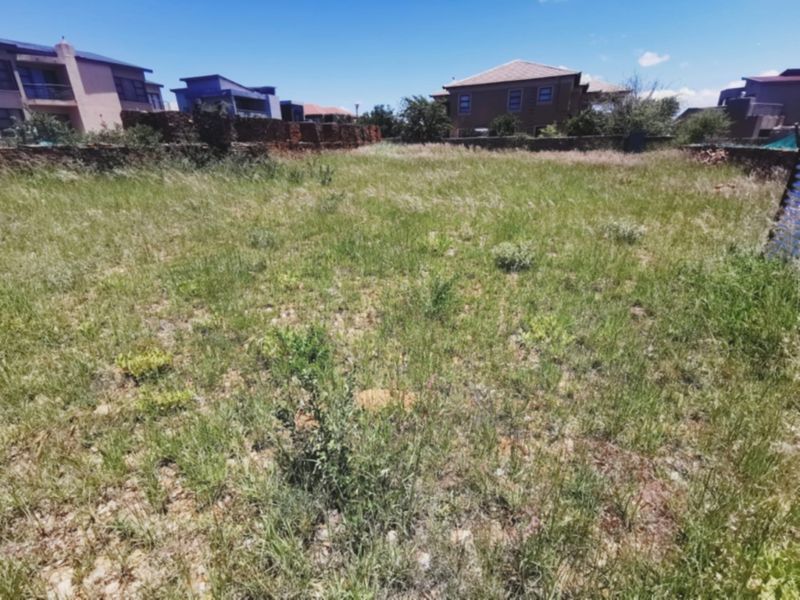 A vacant residential plot featuring overgrown grass and established boundary walls, situated within a developed neighborhood setting.