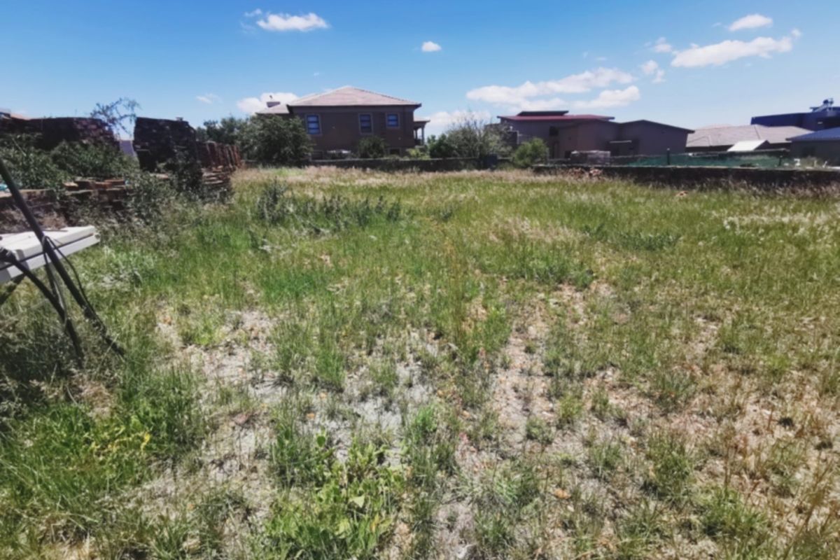 A vacant residential plot featuring overgrown grass and existing boundary walls, situated in a developed neighborhood.