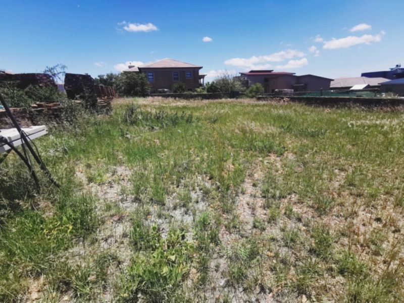 A vacant residential plot featuring overgrown grass and existing boundary walls, situated in a developed neighborhood.