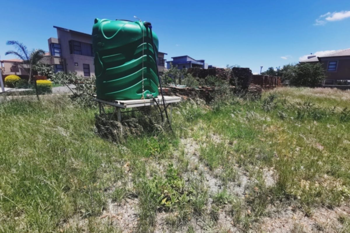 Vacant residential land featuring a green water storage tank on a metal stand and a partially collapsed brick boundary wall.