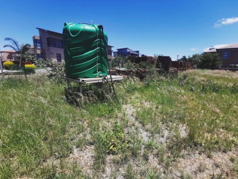 Vacant residential land featuring a green water storage tank on a metal stand and a partially collapsed brick boundary wall.