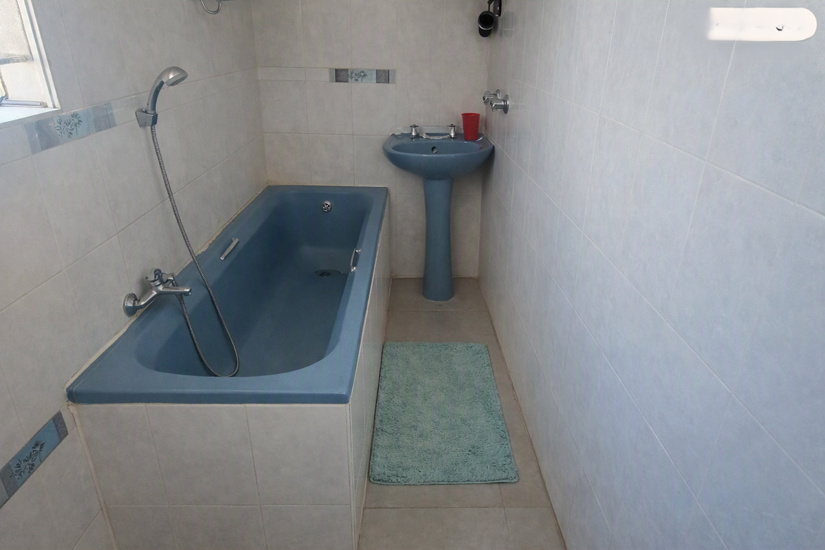 A compact bathroom featuring a blue pedestal basin and matching built-in bathtub with full-height wall tiling.