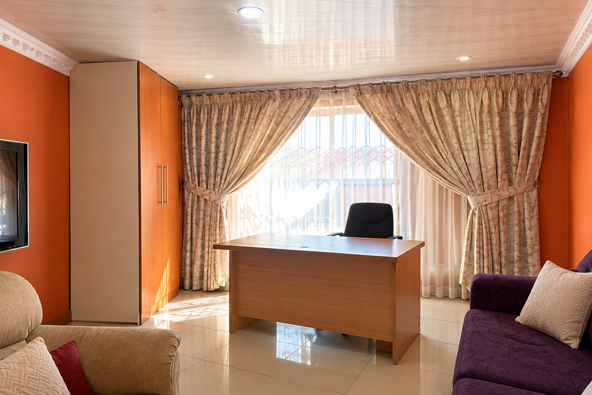 A living room featuring tiled flooring, decorative ceiling cornicing, and a built-in cupboard, with large windows covered by curtains.