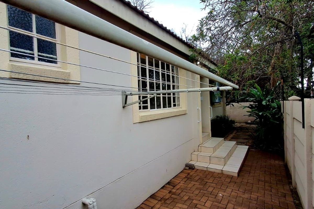 A view of the rear exterior of the townhouse, featuring brick paving, tiled steps leading to the entrance, and a wall-mounted clothesline.
