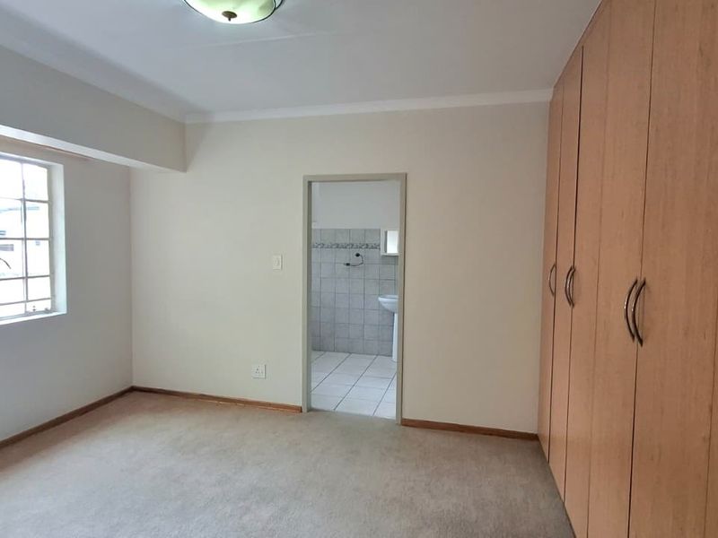 A spacious, empty bedroom featuring neutral carpeting, built-in wooden cupboards, and an adjoining bathroom entrance.
