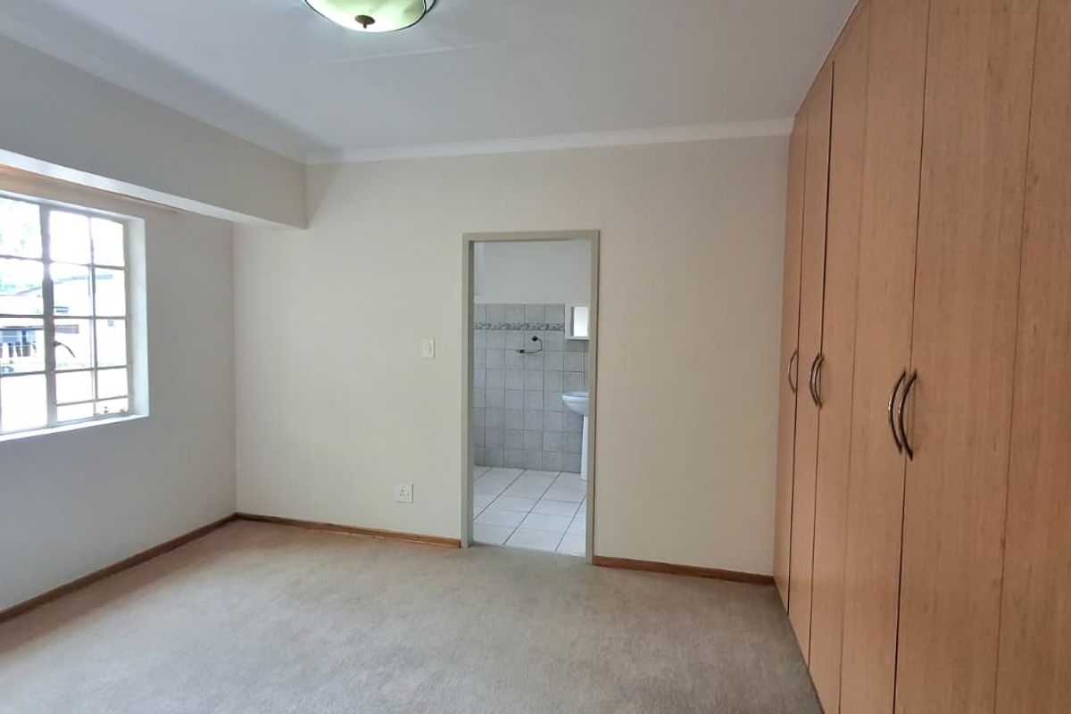 A spacious, empty bedroom featuring neutral carpeting, built-in wooden cupboards, and an adjoining bathroom entrance.