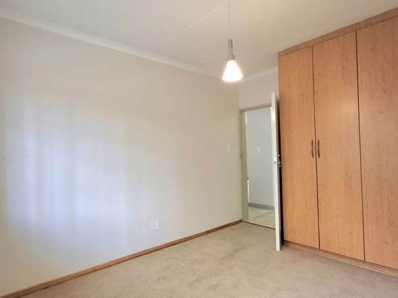 A clean, empty bedroom featuring neutral walls, carpeted flooring, and ample built-in wooden cupboards.