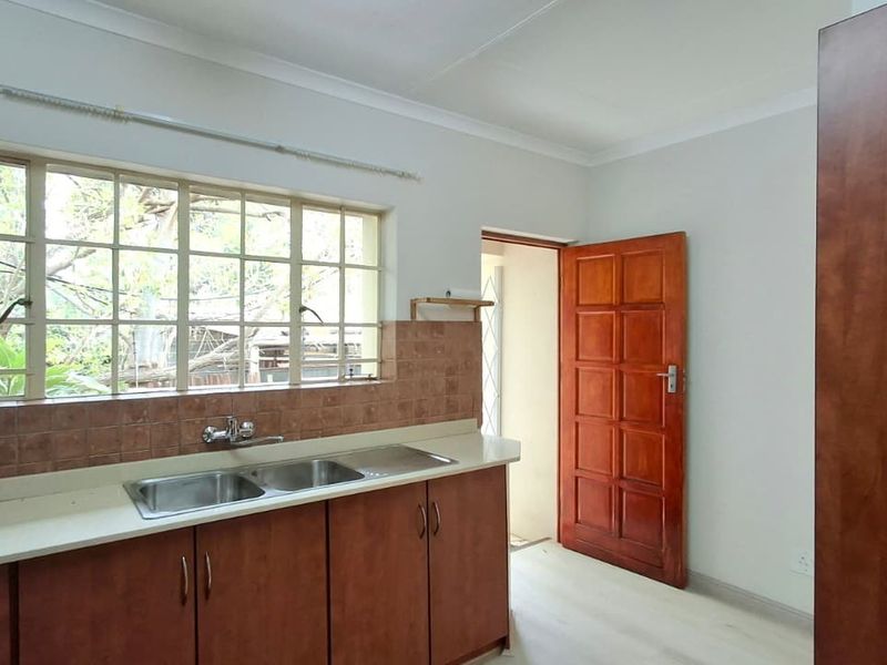 A functional kitchen area featuring laminate cabinetry, a double stainless steel sink, tiled backsplash, and natural light through steel-framed windows.