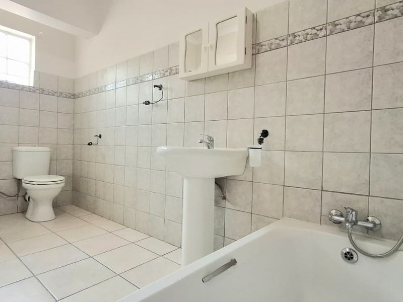 A spacious, tiled bathroom featuring a pedestal basin, bathtub, and separate shower enclosure, currently in need of minor fixture repairs and cosmetic updates.