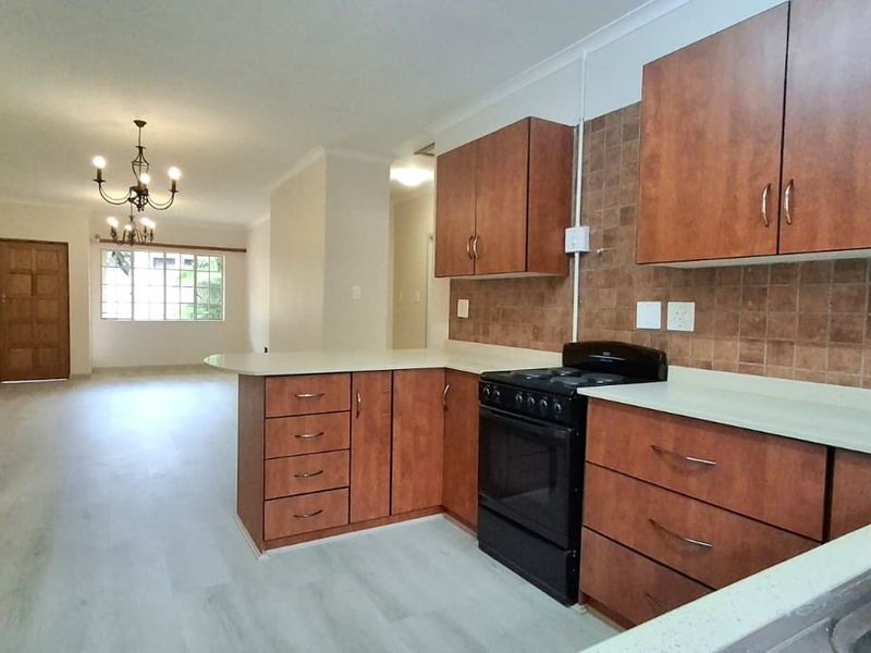 Open-plan kitchen and living area featuring wood-finish cabinetry, tiled backsplash, and light-toned laminate flooring, offering a functional and spacious layout.