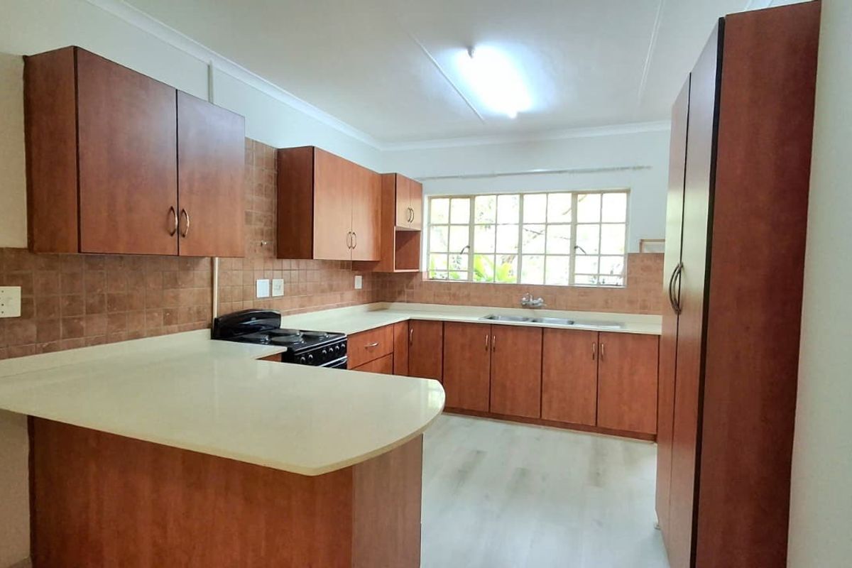 A functional kitchen featuring wood-look laminate cabinetry, ample counter space, a double sink, and a tiled backsplash, offering a clean and practical layout.