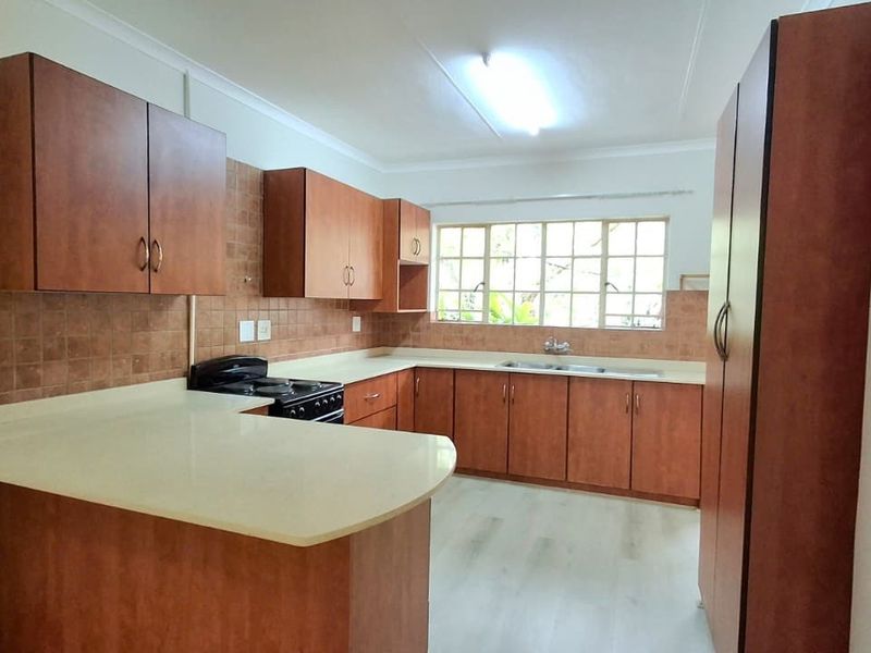 A functional kitchen featuring wood-look laminate cabinetry, ample counter space, a double sink, and a tiled backsplash, offering a clean and practical layout.