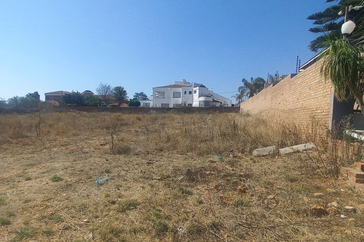A vacant residential plot featuring a brick boundary wall with electric fencing, offering a clear space for future development.