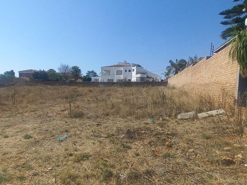 A vacant residential plot featuring a brick boundary wall with electric fencing, offering a clear space for future development.
