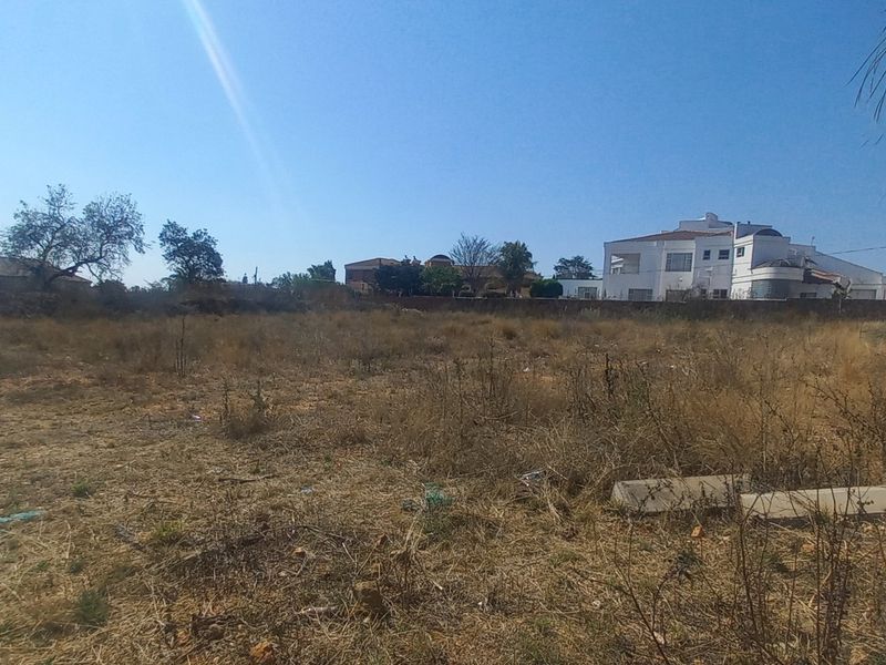 A vacant residential plot featuring dry, overgrown vegetation and a brick boundary wall, offering a blank canvas for future development.